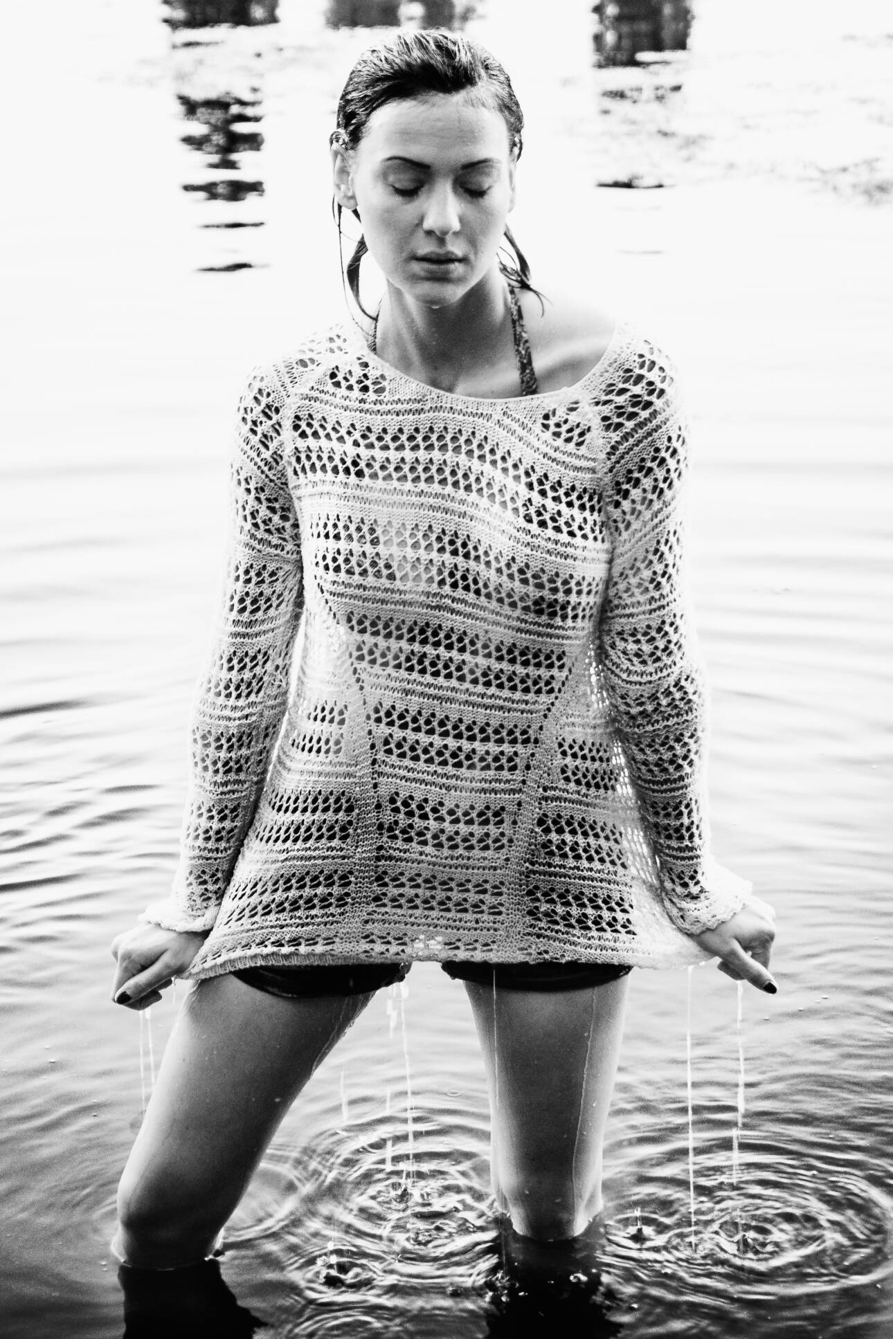 Frau im nassen Strickpullover steht knietief im Wasser, ausdrucksstarkes Schwarzweiß-Portrait