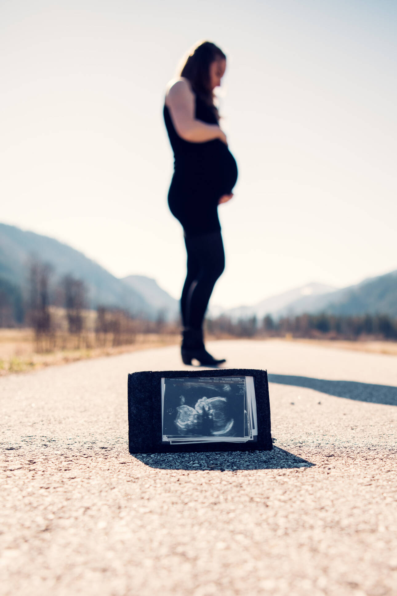 Schwangere hält ihren Babybauch, im Vordergrund Ultraschallbilder vor Bergkulisse