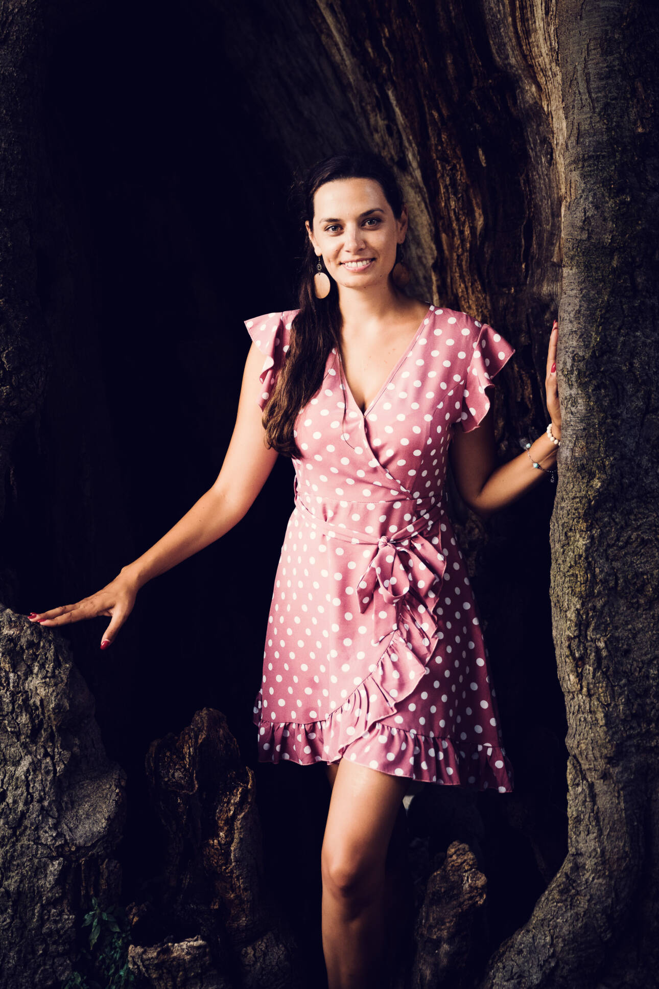 Lächelnde Frau im rosa Punktekleid in der Höhlung eines mächtigen alten Baumstamms